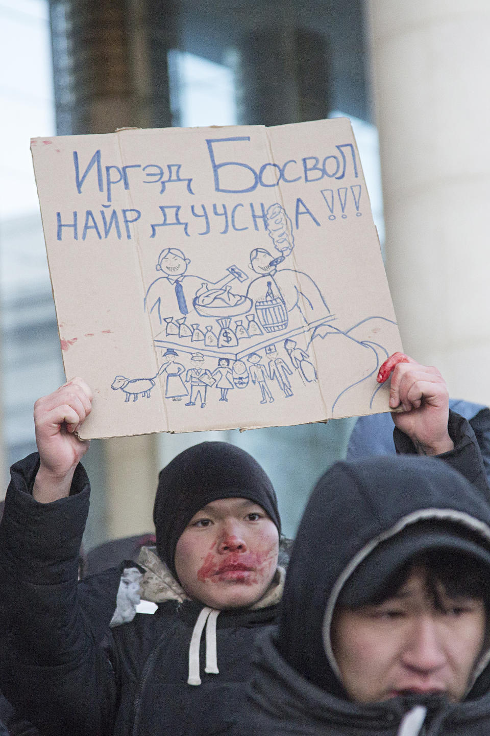 A protester with blood on his face holds up a card which reads "If the citizens rise up, the feast is over" during a protest on Sukhbaatar Square in Ulaanbaatar in Mongolia on Monday, Dec. 5, 2022. Protesters angered by allegations of corruption linked to Mongolia's coal trade with China have stormed the State Palace in the capital, demanding dismissals of officials involved in the scandal. (AP Photo/Alexander Nikolskiy)