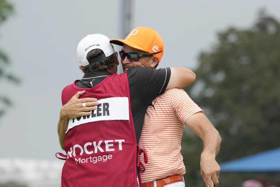 Rickie Fowler is hugged by his caddie Ricky Romano after Fowler's win on the first play-off hole on the 18th green during the final round of the Rocket Mortgage Classic golf tournament at Detroit Country Club, Sunday, July 2, 2023, in Detroit. (AP Photo/Carlos Osorio)