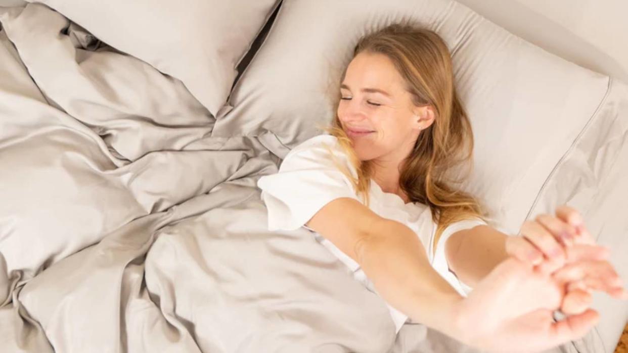 A woman smiling and stretching while lying in bed with Luff Sleep sheets. 