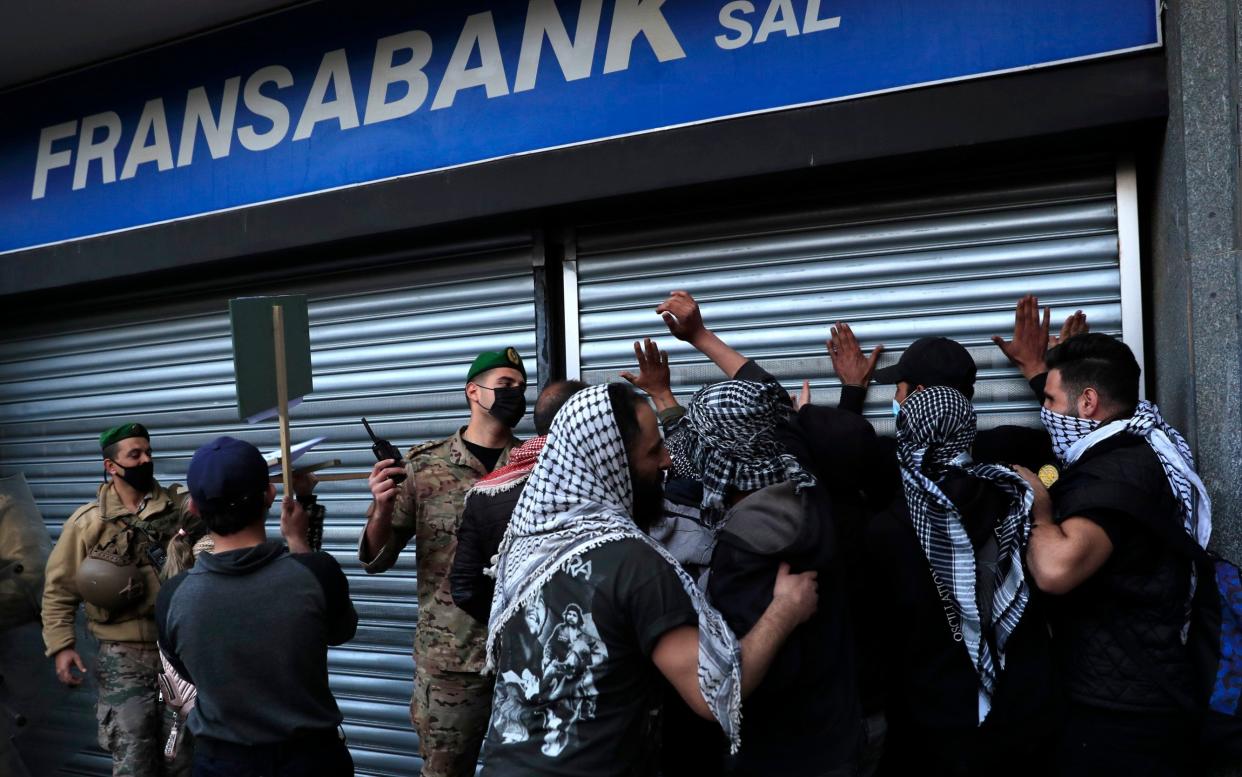 A Lebanese army officer, center, pushes back protesters who were trying to break a bank door, during a protest demanding that local banks allow them to withdraw their money  - Hussein Malla /AP