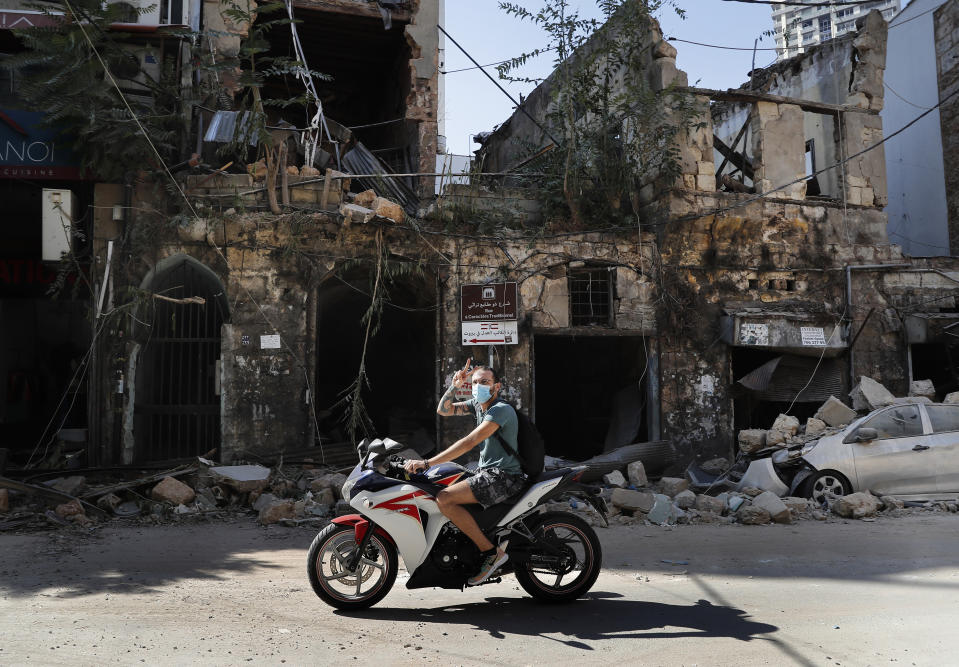 A man rides his motorcycle flashing a victory sign while passing a house destroyed by Tuesday's massive explosion in the seaport of Beirut, Lebanon, Wednesday, Aug. 5, 2020. Residents of Beirut awoke to a scene of utter devastation on Wednesday, a day after a massive explosion at the port sent shock waves across the Lebanese capital, killing at least 100 people and wounding thousands. (AP Photo/Hussein Malla)