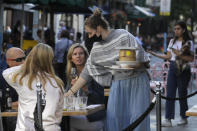 A waitress wears a mask as she serves customers dinning out in London, Monday, Sept. 21, 2020. Britain's top medical advisers have painted a grim picture of exponential growth in illness and death if nothing is done to control the second wave of coronavirus infections, laying the groundwork for the government to announce new restrictions later this week. (AP Photo/Kirsty Wigglesworth)