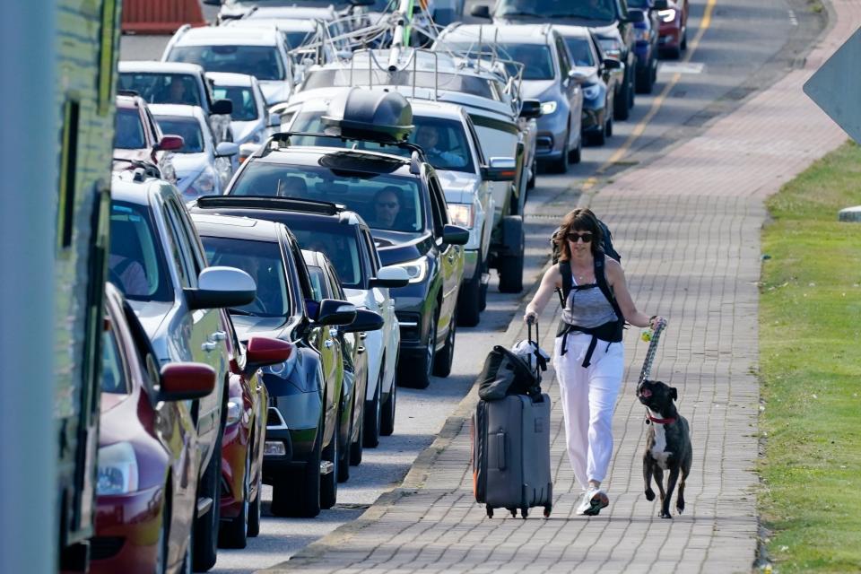 Terri Mills and her dog, Carlos, walk past a line of vehicles waiting to enter Canada at the Peace Arch border crossing in Blaine, Washington on Aug. 9. Mills, an American from Grizzly Flats, Calif., was heading to visit her Canadian husband after Canada opened its border to nonessential travel.