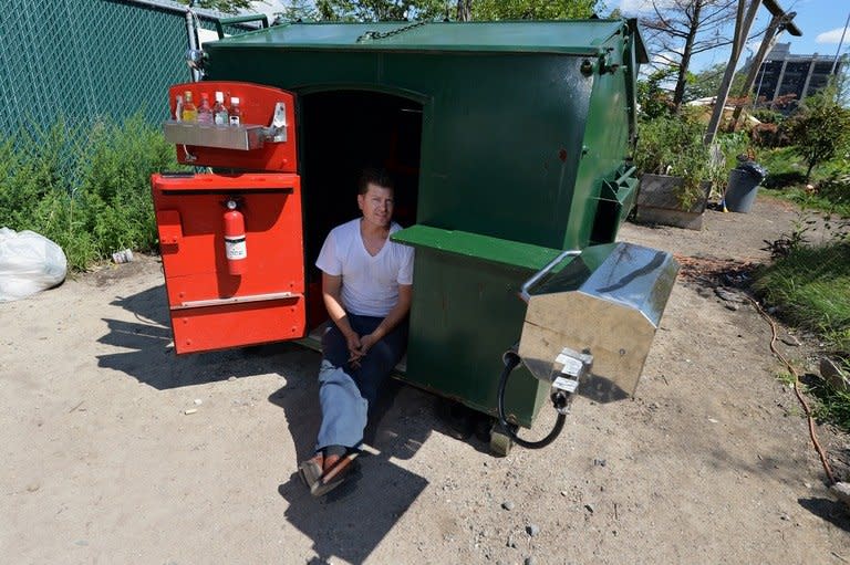 Greg Kloehn sits on the doorstep of the home he made from a trash dumpster August 15, 2013 in New York. A well-stocked minibar, a cushioned sofa and a toilet which can be hooked up to the city's sewer system are all included