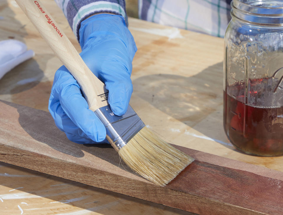 Woman uses a paintbrush to apply Danish oil to a wood board to waterproof it.