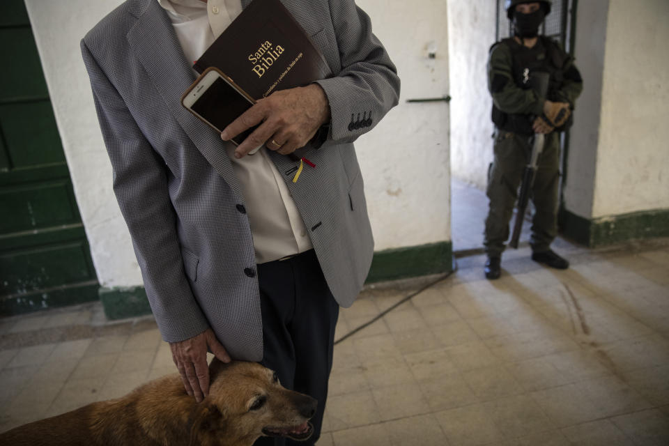 Evangelical Pastor Oscar Sensini, founder of Redil de Cristo church, or "Christ's Sheepfold," clutches his Bible as he pets a prison dog after giving a religious service in the Correctional Institute Model U.I, Dr. Cesar R Tabares, known as Penitentiary Unit 1 in Coronda, Santa Fe Province, Argentina, Friday, Nov. 19, 2021. Sensini's brother David also ministers the jail population. (AP Photo/Rodrigo Abd)