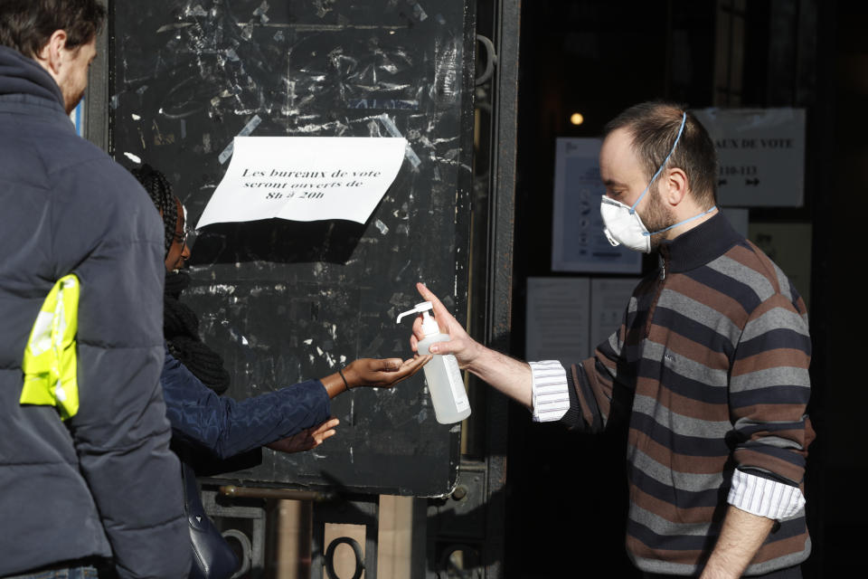 A volunteer sprays hydroalcoholic gel on a voter during the first round of the municipal elections, in Strasbourg, eastern France, Sunday March 15, 2020. The new virus has shuttered all schools, banished cheek-kissing and upended daily life across France, but President Emmanuel Macron won't let it disrupt democracy, so he's maintaining nationwide elections this weekend. For most people, the new coronavirus causes only mild or moderate symptoms. For some it can cause more severe illness. (AP Photo/Jean-Francois Badias)