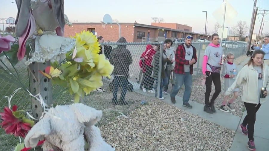 A line of people walking beside a flower memorial