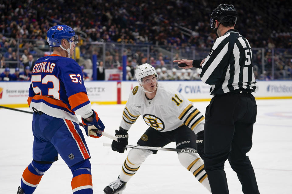Boston Bruins center Trent Frederic (11) speaks to linesman Andrew Smith before a faceoff against New York Islanders center Casey Cizikas (53) during the first period of an NHL hockey game in Elmont, N.Y., Friday, Dec. 15, 2023. (AP Photo/Peter K. Afriyie)