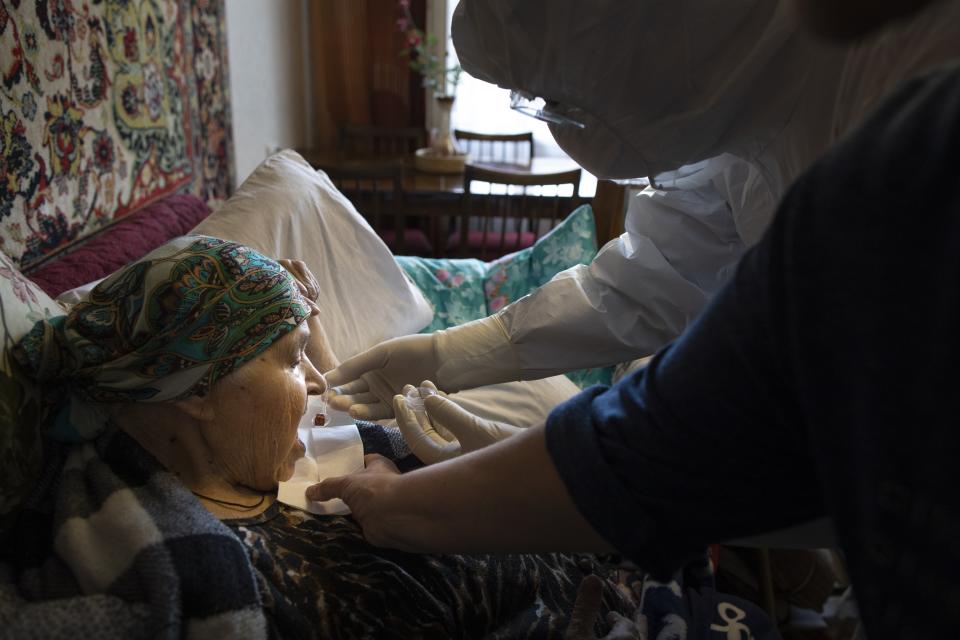 In this photo taken on Tuesday, May 26, 2020, Father Vasily Gelevan, wearing a biohazard suit and gloves to protect against the coronavirus, gives Holy Communion to Serafima Matveyeva, 92, who is suspected of being infected with the coronavirus, at her apartment in Moscow, Russia. In addition to his regular duties as a Russian Orthodox priest, Father Vasily visits people infected with COVID-19 at their homes and hospitals. (AP Photo/Alexander Zemlianichenko)