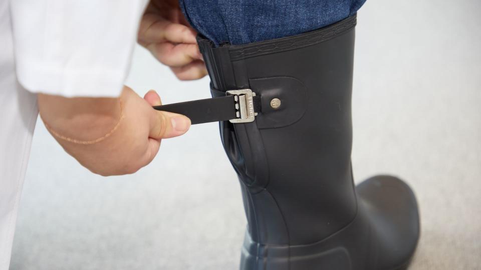 a person tightening the buckle on the back of black boots as part of good housekeeping's testing for the best rain boots for women