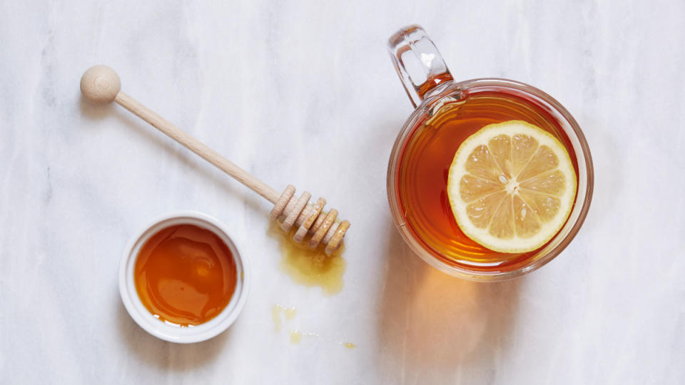 A mug of tea with a slice of lemon and a bowl of honey beside it, which is good for a cough