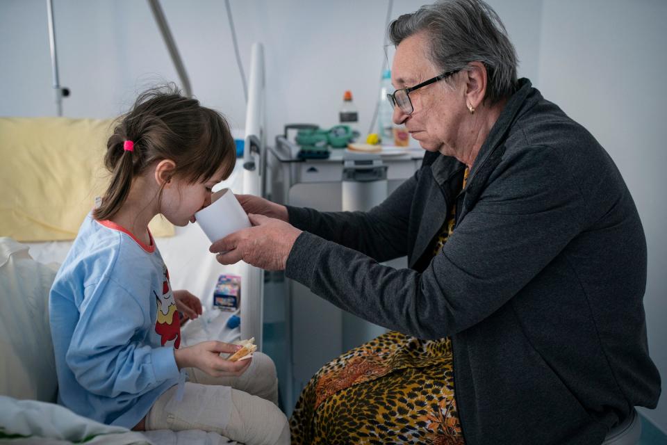 Evheniia Ukhvatova, 6, of Dnipro, Ukraine, left, gets a hand with her breakfast from her great grandmother Valentina Ukhvatova, 75, as she recovers in her hospital room at the Independent Public Health Care Facility in Leczna, Poland on Tuesday, May 16, 2023  after having laser surgery and skin grafts to treat burns on the back of her legs and feet she sustained in a house fire in 2020.