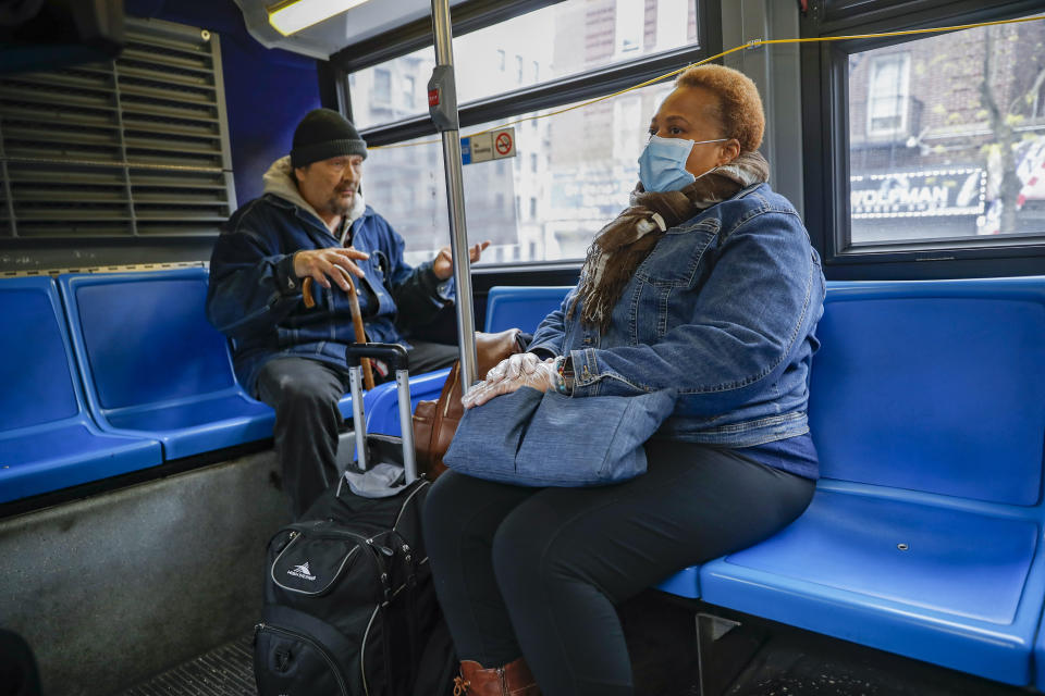 In this Thursday, April 23, 2020 photo, Ruth Caballero, a nurse with The Visiting Nurse Service of New York, right, attempts to reason with a fellow bus passenger who refuses to wear a face mask as she commutes by bus on her rounds in upper Manhattan in New York. Home care nurses, aides and attendants, who normally help an estimated 12 million Americans with everything from bathing to IV medications, are now taking on the difficult and potentially dangerous task of caring for coronavirus patients. (AP Photo/John Minchillo)