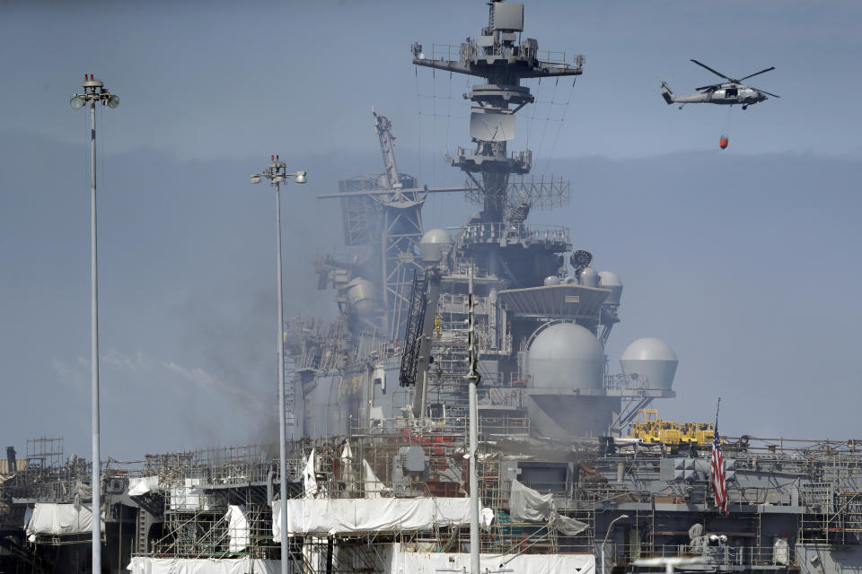 A helicopter carrying water passes the USS Bonhomme Richard, Tuesday, July 14, 2020, in San Diego. The battle to save the ship from a ravaging fire entered a third day in San Diego Bay on Tuesday with indications that the situation aboard the amphibious assault ship was improving. The U.S. Navy said in a statement late Monday that firefighters were making significant progress with the assistance of water drops by helicopters. (AP Photo/Gregory Bull)