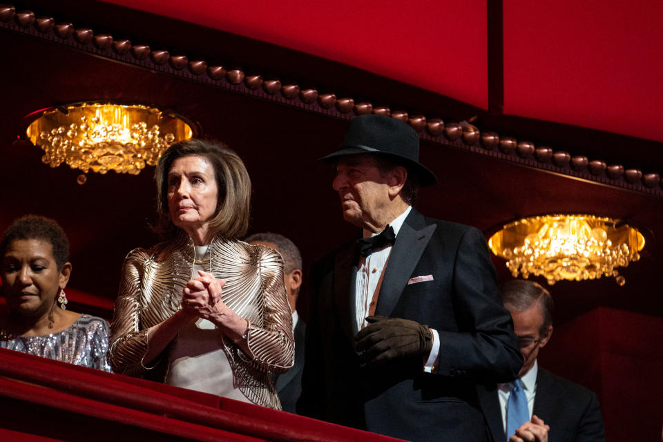 A gowned Nancy Pelosi and her husband, a tuxedoed Paul Pelosi, who is wearing a hat and glove following his recovery from the attack, stand while attend the Kennedy Center Honors gala.