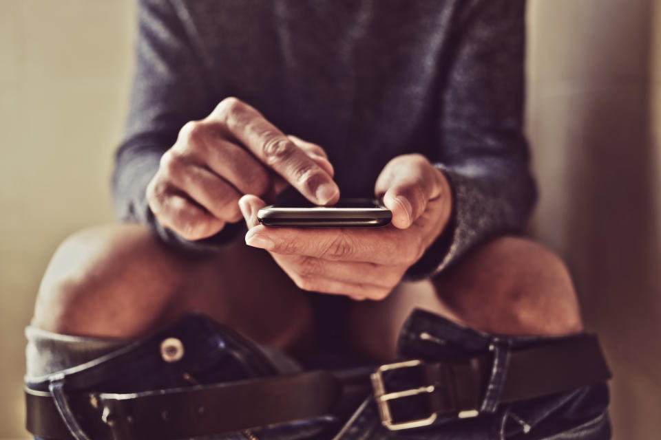 closeup of a young caucasian man using his smartphone in the toilet while sitting in the bowl