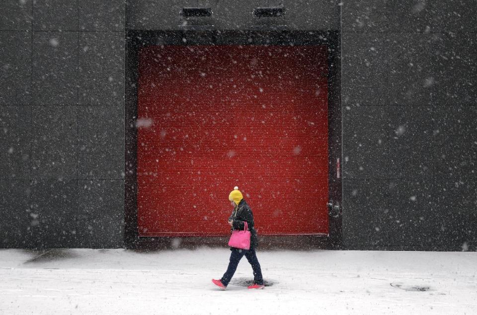 A woman walks outside of an office building as snow falls, Tuesday, Jan. 21, 2014, in Baltimore. Thousands of flights were canceled, students got an extra day off from school or were being sent home early, and the federal government closed its offices in the Washington area Tuesday as another winter storm bore down on the Mid-Atlantic and Northeast. (AP Photo/Patrick Semansky)