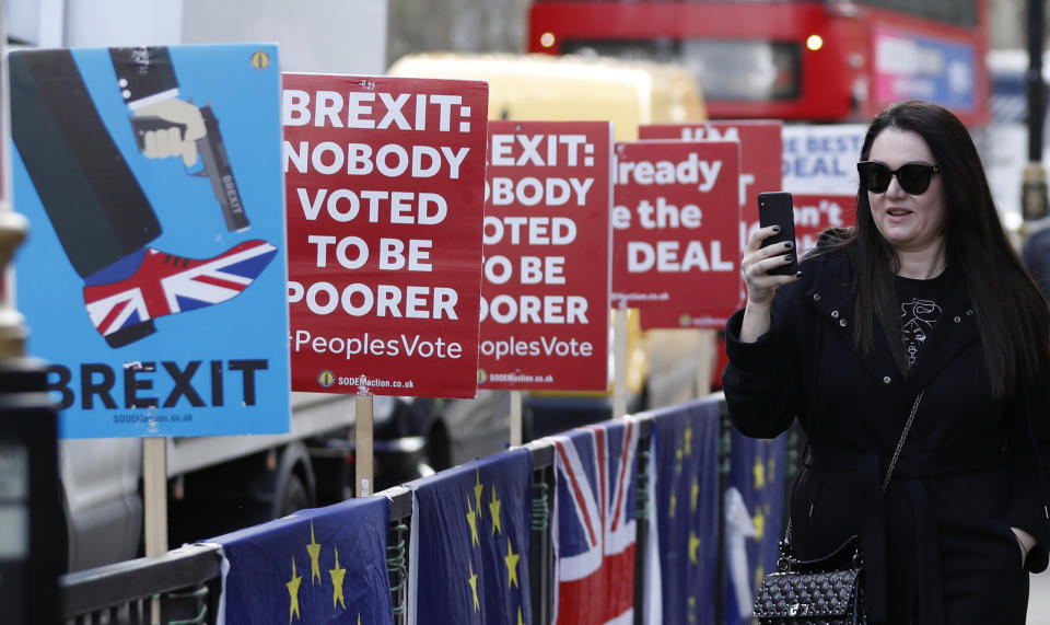 A woman takes pictures on her smart phone as she walks past anti-Brexit placards near the House of Parliament in London, Tuesday, March 26, 2019. British Prime Minister Theresa May's government says Parliament's decision to take control of the stalled process of leaving the European Union underscores the need for lawmakers to approve her twice-defeated deal. (AP Photo/Alastair Grant)