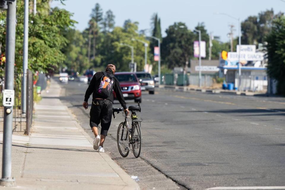 A bicyclist walks his bike along Franklin Boulevard earlier this month. The Franklin Boulevard Complete Street project, set to begin construction in 2024, plans to add protected bike lanes, wider sidewalks, better street lighting and more shade trees to the North City Farms neighorhood in Sacramento.