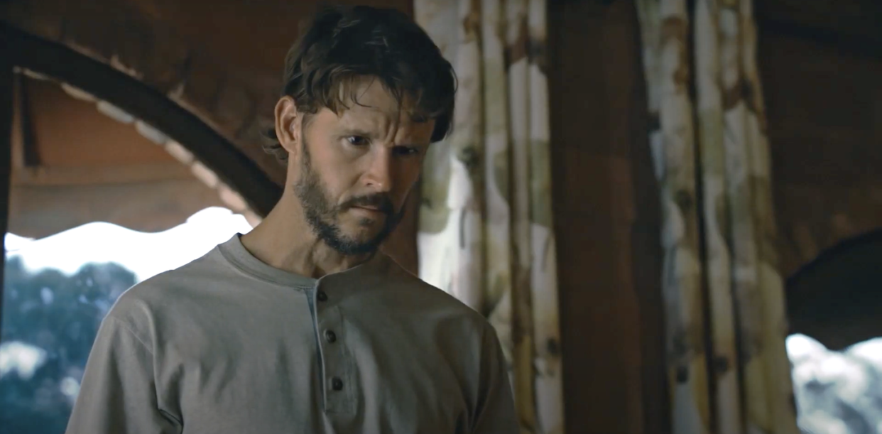 ryan kwanten as alex in the portrait, a man with a beard stands inside a cabin