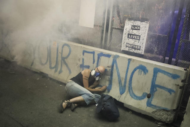 FILE - A demonstrator hides under a barrier as federal officers release tear gas during a Black Lives Matter protest at the Mark O. Hatfield United States Courthouse, July 29, 2020, in Portland, Ore. More than 119,000 people have been injured by tear gas and other chemical irritants around the world since 2015 and some 2,000 suffered injuries from "less lethal" impact projectiles, according to a new report released Wednesday, March 22, 2023. (AP Photo/Marcio Jose Sanchez, File)