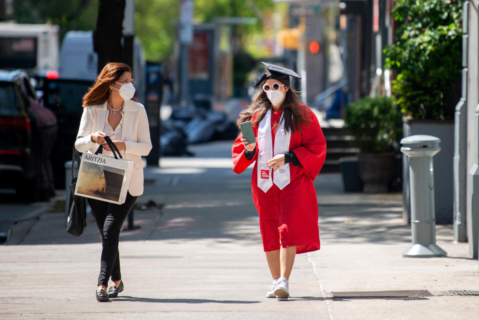 A mother wearing a mask walks with her daughter wearing a mask, cap and gown amid the coronavirus pandemic on May 14, 2020 in New York City. (Photo by Alexi Rosenfeld/Getty Images)