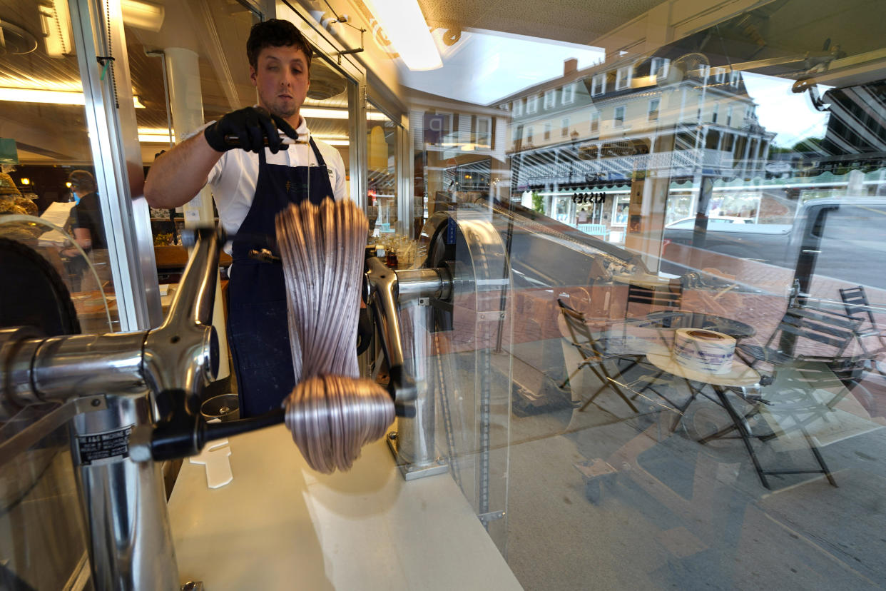 Tyler Melanson makes taffy in the front window of The Goldenrod, a popular restaurant and candy shop, Wednesday, June 1, 2022, in York Beach, Maine. Many businesses are struggling to find enough workers before the busy tourism season. (AP Photo/Robert F. Bukaty)