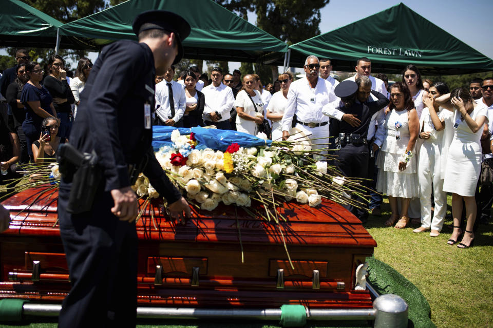 Los Angeles Police Department officers place flowers on fellow Officer Juan Jose Diaz's coffin and hug his family during his funeral at Forest Lawn Hollywood Hills cemetery, Monday, Aug. 12, 2019, in Los Angeles. Diaz was killed while off duty in Lincoln Heights after visiting a taco stand. (Sarah Reingewirtz/The Orange County Register via AP)