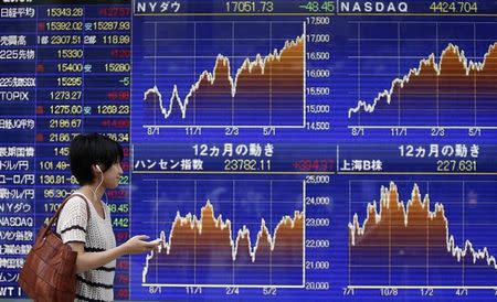 A pedestrian holding her mobile phone looks at an electronic board showing graphs of various countries' stock market indices outside a brokerage in Tokyo July 22, 2014. REUTERS/Yuya Shino