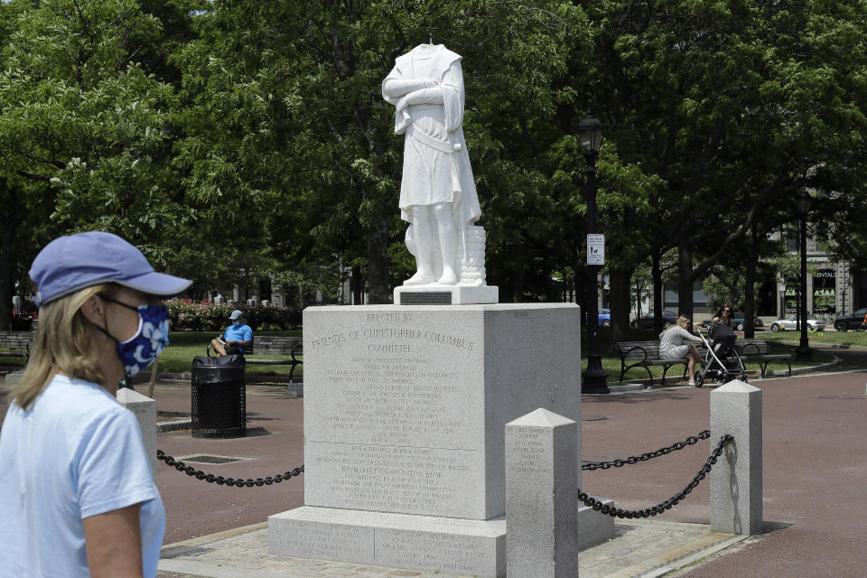 A passer-by walks near a damaged Christopher Columbus statue, Wednesday, June 10, 2020, in a waterfront park near the city's traditionally Italian North End neighborhood, in Boston. The statue was found beheaded Wednesday morning, Boston Mayor Marty Walsh said. (AP Photo/Steven Senne)