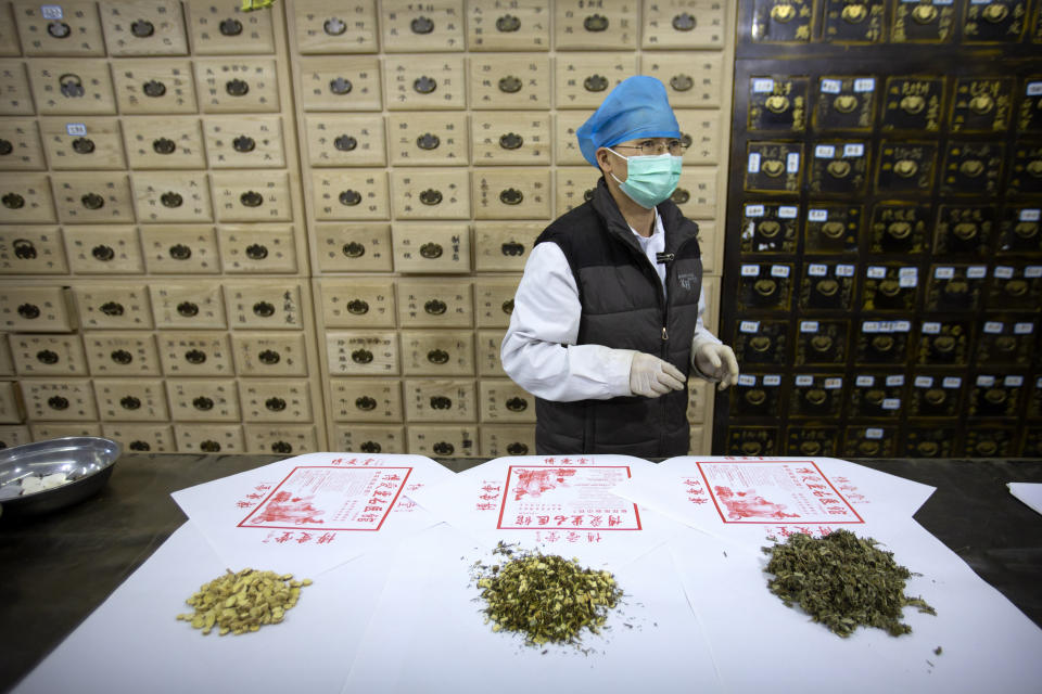 In this March 13, 2020 photo, a worker stands near piles of, from left, Mongolian milkvetch, celery sagebrush, and Chinese mugwort at the Bo Ai Tang traditional Chinese medicine clinic in Beijing. The clinic has prescribed the three herbal ingredients to COVID-19 patients. With no approved drugs for the new coronavirus, some people are turning to alternative medicines without evidence that they work. (AP Photo/Mark Schiefelbein)
