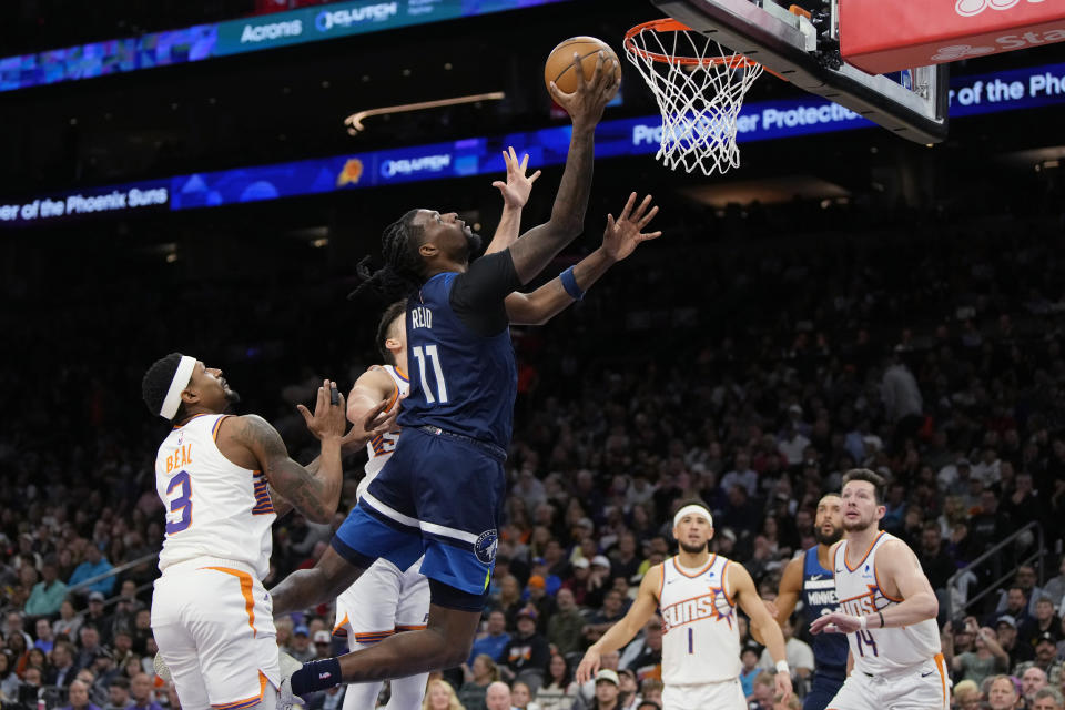 Minnesota Timberwolves center Naz Reid drives between Phoenix Suns guard Bradley Beal (3), guard Devin Booker (1) and forward Drew Eubanks during the second half of an NBA basketball game Friday, April 5, 2024, in Phoenix. (AP Photo/Rick Scuteri)