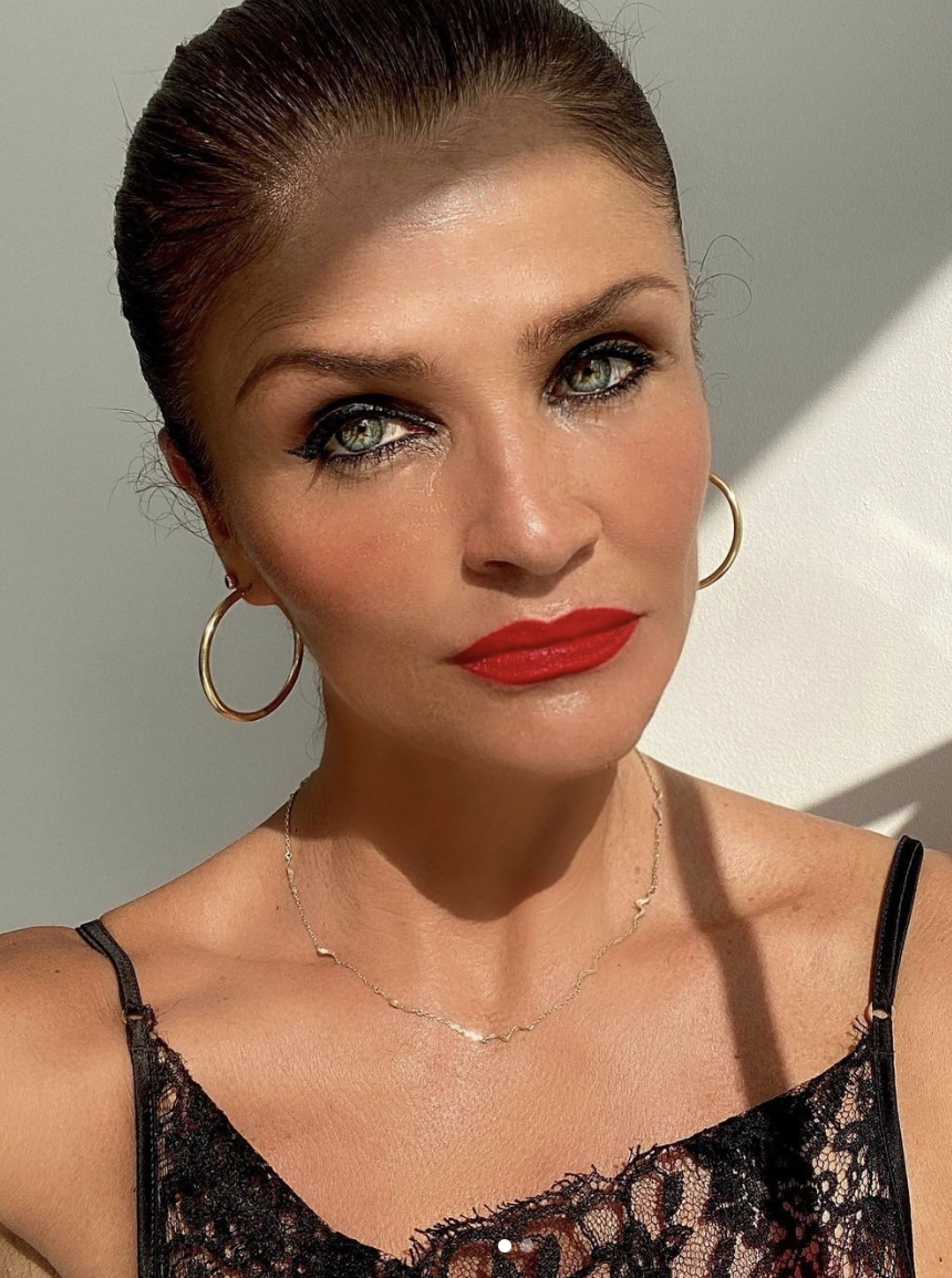 A close-up of Helena Christensen wearing red lipstick and a lacy top. 