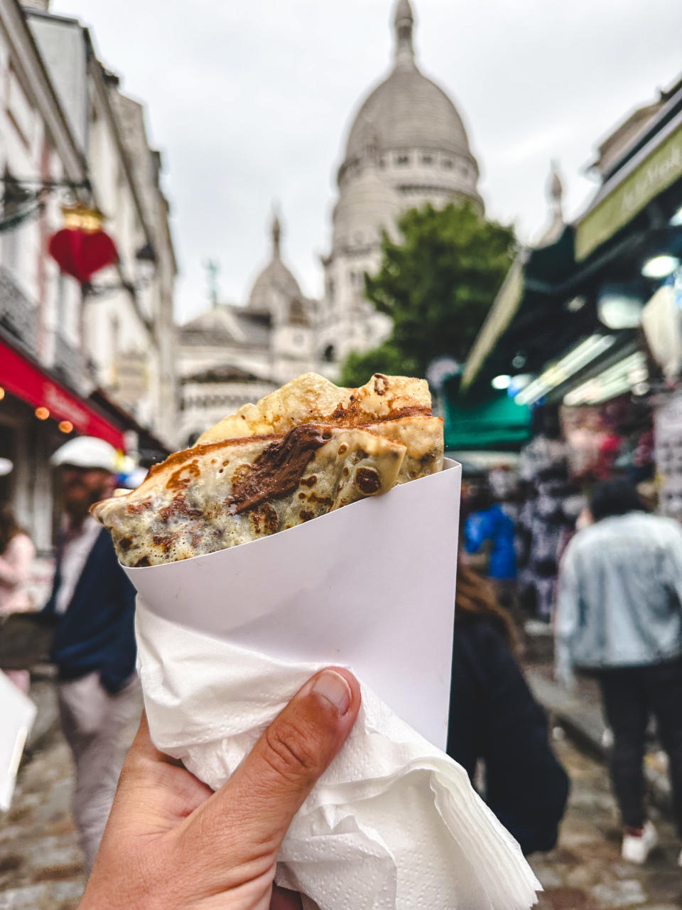 A person holding a crepe with the Sacré-Cœur Basilica in the distant background