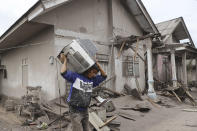 A man carries a television as he evacuates to a safer place following the eruption of Mount Semeru in Lumajang district, East Java province, Indonesia, Monday, Dec. 6, 2021. The highest volcano on Java island spewed thick columns of ash into the sky in a sudden eruption Saturday triggered by heavy rains. Villages and nearby towns were blanketed and several hamlets buried under tons of mud from volcanic debris. (AP Photo/Trisnadi)