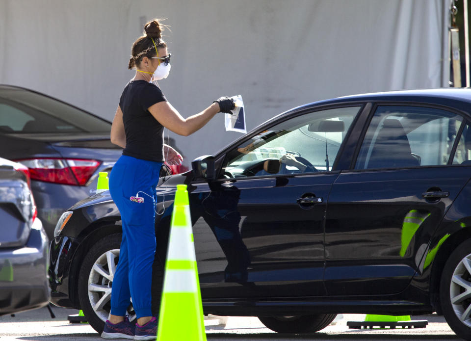 A health care worker direct a person to use a swab for a self administered test at the Miami-Dade County Youth Fairgrounds at Tamiami Park, on Sunday, Nov. 29, 2020 in Miami. (David Santiago/Miami Herald via AP)