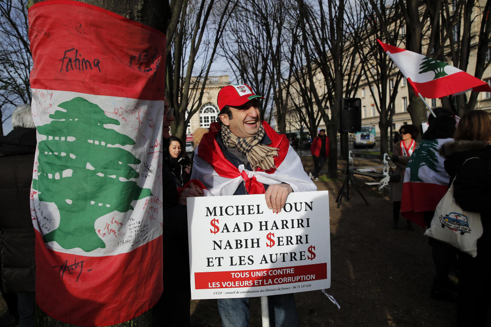 Lebanese protester holds a placard with names of politicians reading "all united against thieves and corruption" during a gathering outside of the French foreign ministry in Paris, Wednesday, Dec. 11, 2019, to denounce a closed-door meeting of diplomats from several countries on aid to Lebanon. The Middle Eastern country is facing a political and economic crisis, and the international group is discussing conditions for global assistance to help ease Lebanon's financial woes.(AP Photo/Francois Mori)