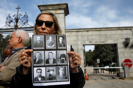 Silvia Navarro, a member of an organisation representing family members of civil war victims who have demanded to have their relatives exhumed, poses with a banner showing pictures of victims outside the entrance to the Basilica of the Valley of the Fallen (Valle de los Caidos), the giant mausoleum holding the remains of dictator Francisco Franco and over 30,000 civil war dead, where a scientific team entered to search for the remains of four of the dead for the first time after a court order approved the exhumation of two victims, Manuel and Antonio Lapena, executed in 1936 by Franco's forces during the Spanish Civil War, in San Lorenzo de El Escorial, Spain, April 23, 2018. REUTERS/Juan Medina