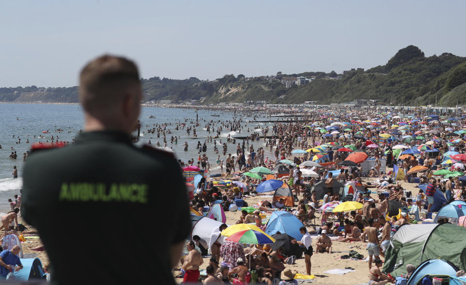 A member of the Ambulance service looks out at people crowded on the beach in Bournemouth, England, Thursday June 25, 2020, as coronavirus lockdown restrictions have been relaxed. According to weather forecasters Thursday could be the UK's hottest day of the year, so far, with scorching temperatures forecast to rise even further. (Andrew Matthews/PA via AP)