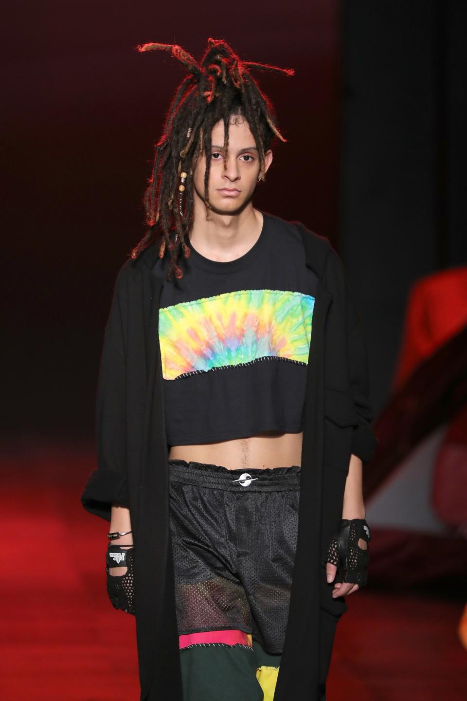 A model with dreadlocks wears a loose black tee with tie-dye design.