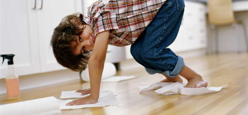 A kid with paper towels wiping up spill on floor.