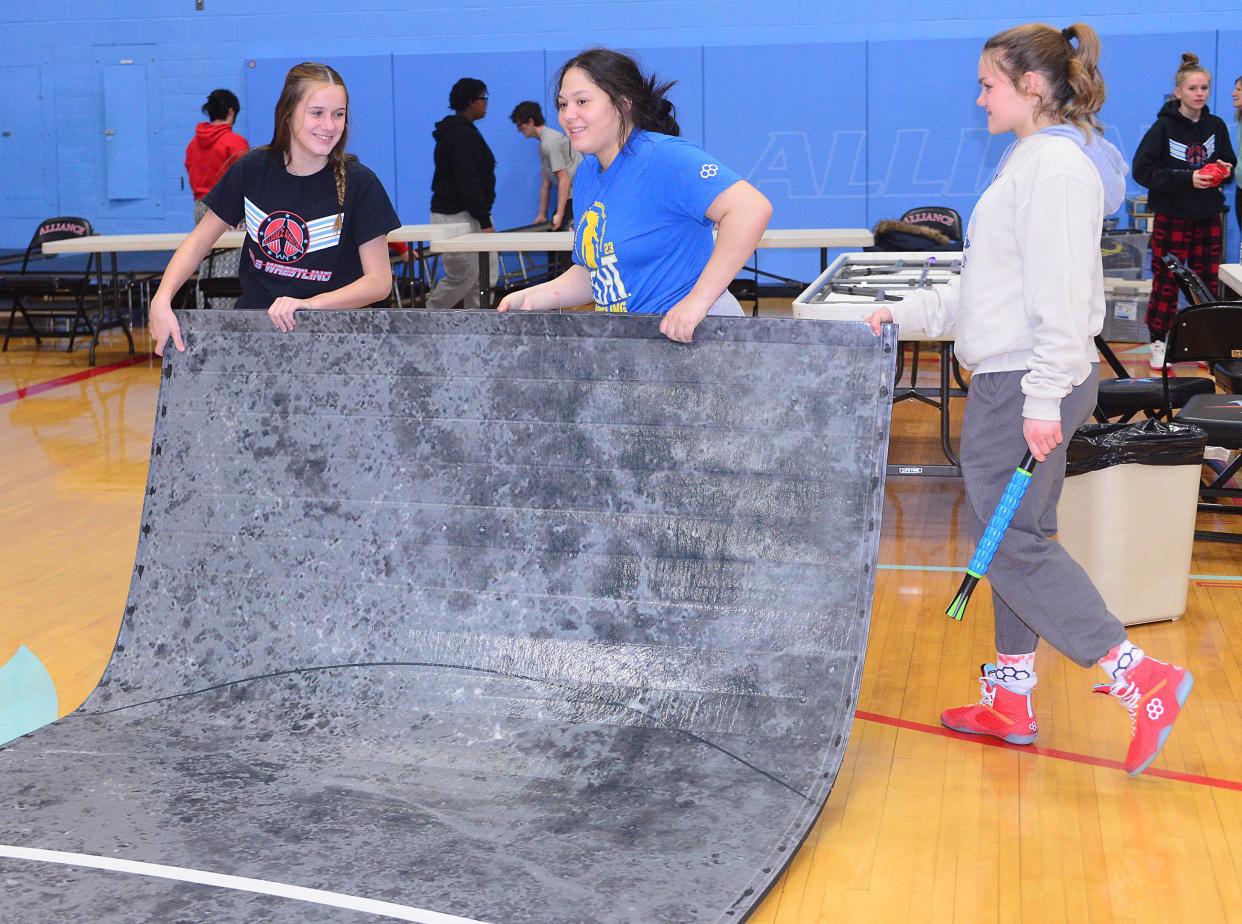 Members of the Alliance High School girls wrestling team, from left, Miley Gross, Isabella Hall and Avery Horning assist with the steup for the 2024 Top Gun Tournament on Thursday, Jan. 11, 2024 in the Alliance High School gymnasium.