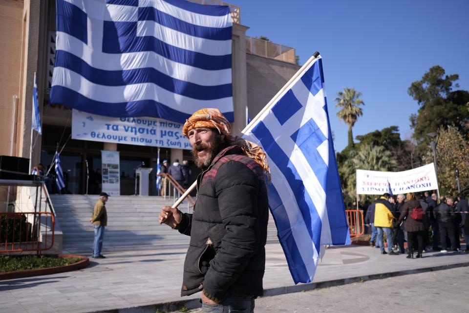 A protester holds a Greek flag outside the Municipality of Mytilene during a rally on the northeastern Aegean island of Lesbos, Greece, on Wednesday, Jan. 22, 2020. Local residents and business owners have launched a day of protest on the Greek islands hardest hit by migration, demanding the Greek government ease severe overcrowding at refugee camps. (AP Photo/Aggelos Barai)