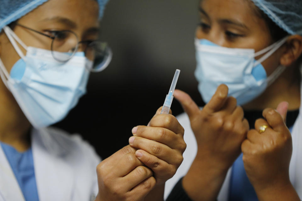 A Nepalese health worker, right, instructs another on administering COVID-19 vaccine at Teaching Hospital in Kathmandu, Nepal, Wednesday, Jan. 27, 2021. Thousands of health workers lined up across Nepal to get the coronavirus vaccine Wednesday as the Himalayan nation began its campaign to get the population vaccinated within three months. Neighboring India gifted Nepal 1 million doses of the AstraZeneca-Oxford University vaccine manufactured under license by the Serum Institute of India. (AP Photo/Niranjan Shrestha)