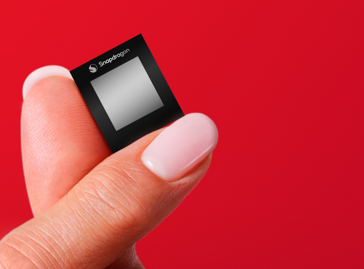  Two fingers holding up Qualcomm Snapdragon chip against a red background. 