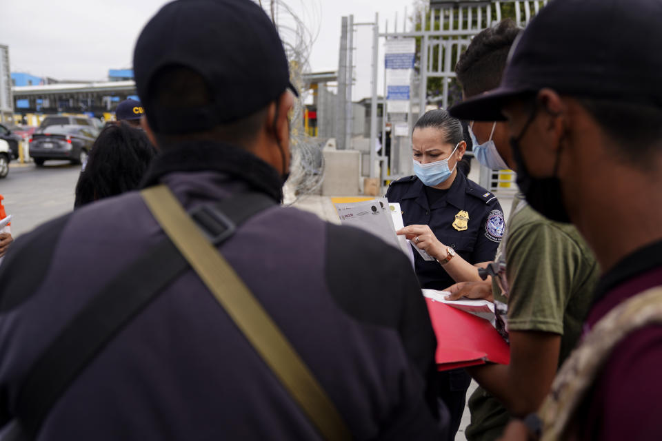 A United States Customs and Border Protection officer examines paperwork of migrants waiting to cross into the United States to begin the asylum process Monday, July 5, 2021, in Tijuana, Mexico. Dozens of people are allowed into the U.S. twice a day at a San Diego border crossing, part of a system that the Biden administration cobbled together to start opening back up the asylum system in the U.S. Immigration advocates have been tasked with choosing which migrants can apply for a limited number of slots to claim humanitarian protection. (AP Photo/Gregory Bull)