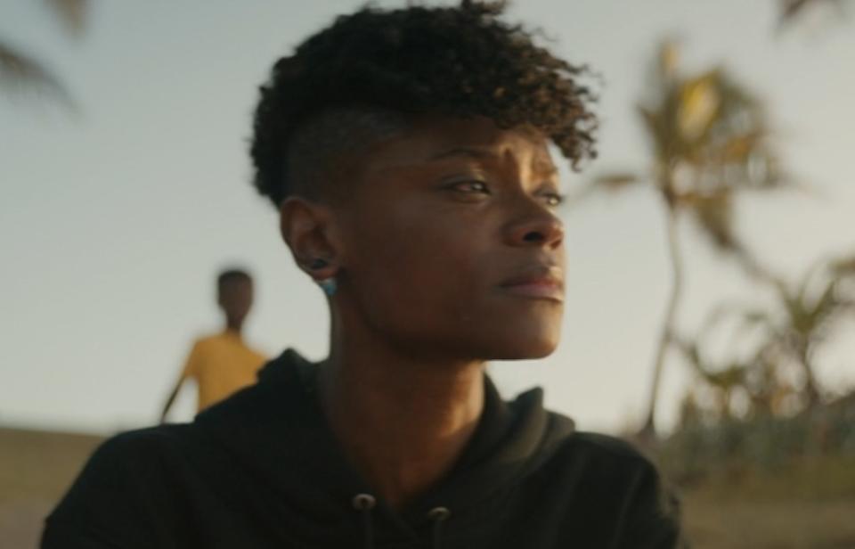 A woman sits on the beach, looking somber