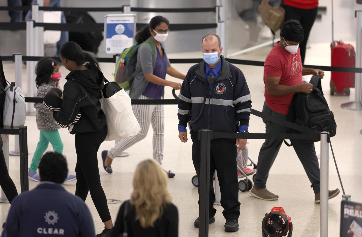 A masked passenger with one child in a stroller and one following her passes a Covenant Aviation Security officer in a stream of airline passengers.