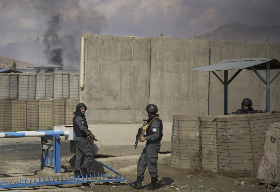 Afghan policemen take position while smoke from a burning building billows in the background as Taliban militants attacked the main Afghan election commission's headquarters in the outskirts of Kabul, Afghanistan, firing on the compound with rocket-propelled grenades and heavy machine guns from a house outside its perimeter wall, Saturday, March 29, 2014. Dozens of employees and other people who had been inside the Independent Election Commission compound took cover in the basement, and no casualties were reported. But two warehouses were hit and set on fire, witnesses said. (AP Photo/Anja Niedringhaus)